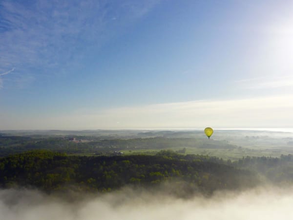 A yellow hot air balloon floats over a green landscape covered in mist.